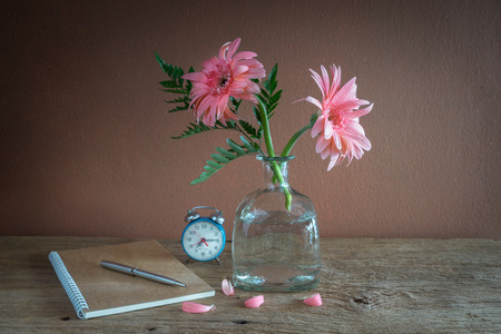 Still life with pink flowers in bottle, alarm clock and note bookの写真素材