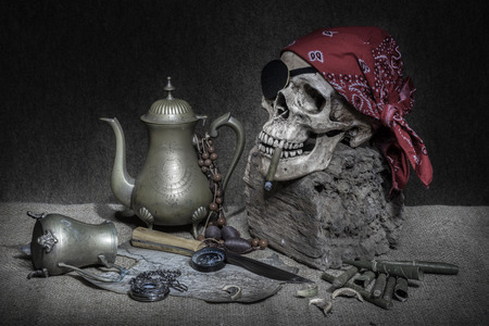 Still life, pirate skull with cigar in the mouth, compass on ancient map, knife and pocket watch hang on the logの写真素材