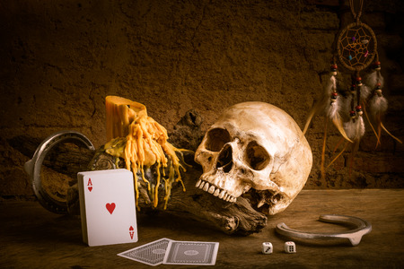 Still life with human skull , candle with wax tear, horseshoe, dream catcher, dice and playing card on grunge brick wallの写真素材