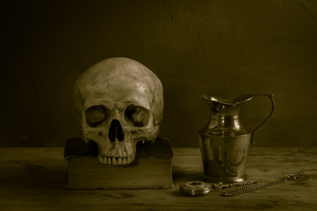 Still life with human skull on old book, vintage brass teapot and pocket watchの写真素材