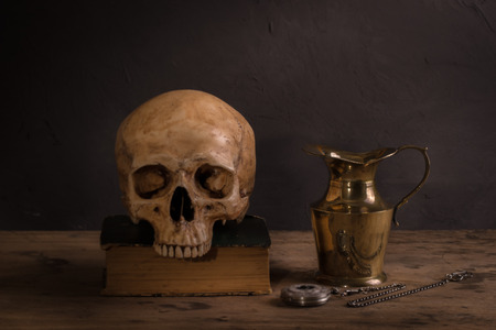 Still life with human skull on old book, vintage brass teapot and pocket watchの写真素材