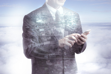 Double exposure of city and business man using smart phone on the cloudの写真素材