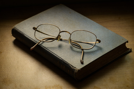 old book open on a wooden table with glassesの写真素材