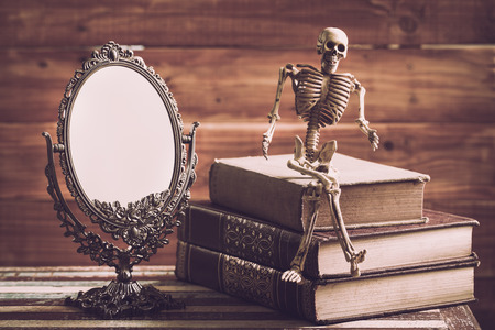 Classic mirror with old books and skelaton on wooden table, vintage styleの写真素材