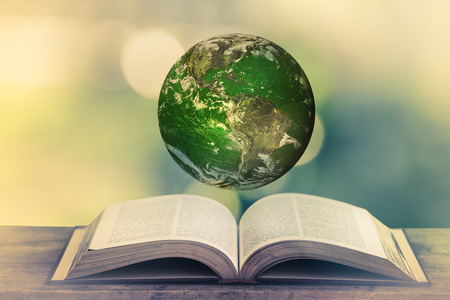 Planet over the open book on a wooden table in nature, green blurry background. World Environment Day. World Mental Health Day concept. Elements of this image furnished by NASA.の写真素材