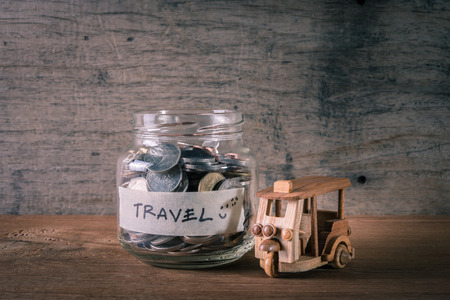 Coins in glass bottle with wooden taxi toy on table, concept for saving money for travelの写真素材