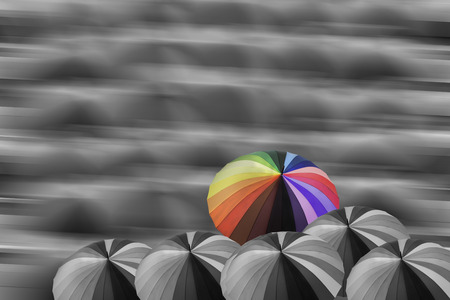 Multicolor umbrella on non-color group of umbrella with motion blurred background, concept to defferent ideaの写真素材