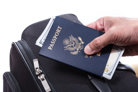 Money in US passport in hand with suitcase, using money for travel around the world conceptの写真素材