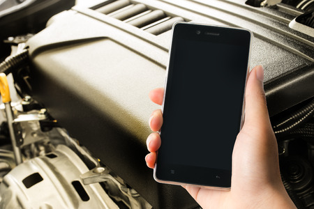 A man holding modern smart phone with blank screen in hand with motor engine backgroundの写真素材