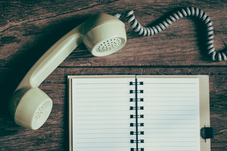 Old telephone with note book on weathered wood background, still life with vintage effectの写真素材