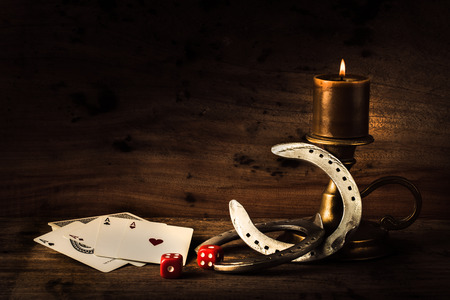 Lucky craps game dice rolling out chance number five and vintage poker cards with winning aces by old horseshoes for player and gambler good luck charm on rustic wood table in western gambling saloonの写真素材