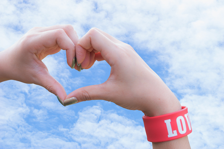 Female hands in form of heart on blue sky and white clouds backgroundの写真素材