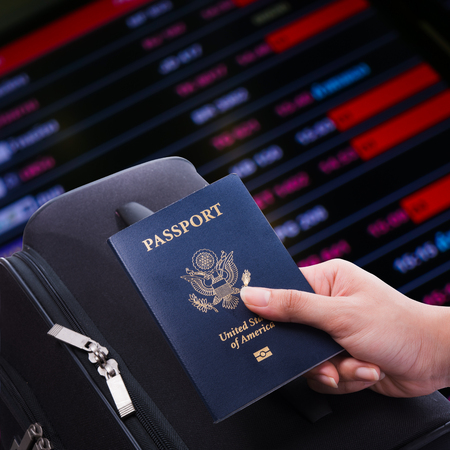 Woman hold US passport in hand with luggage on flight schedule backgroundの写真素材