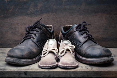Brown shoes of daddy and son on on wooden table, bar or counter over brown wood wall background, fathers day conceptualの写真素材