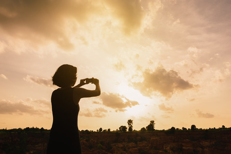 Silhouette woman taking photo with smart phone of landscape,High key.の写真素材