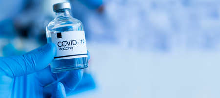 close up The scientist's hand holding covid-19 vaccine dose on color white and blue background has copy space on the right.の写真素材