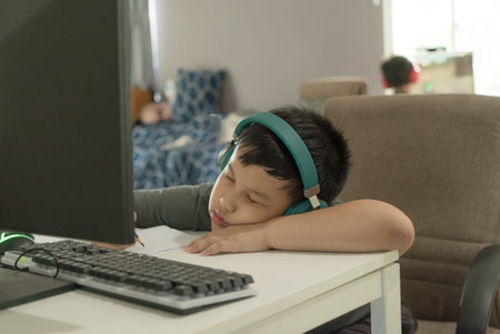 Tired Asian school boy fall asleep during online learning course, boring homeschooling during school...