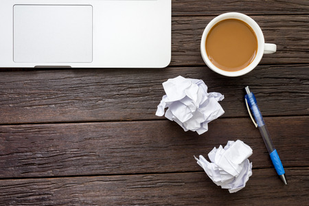 Working with crumpled paper, notebook, coffee cup, and pen on wooden table backgroundの写真素材