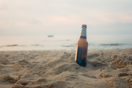 brown bottle of beer standing upright at beach in morningの写真素材