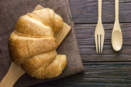 croissant and wooden plate with napkin on wooden table near wooden cutlery,top viewの写真素材