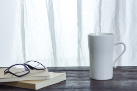 white cup and reading device on wooden desk with window lightの写真素材