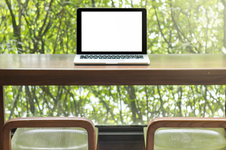 laptop computer on wooden table with bright window light at morning in workplace blur backgroundの写真素材