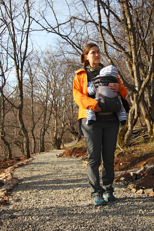 mother with baby in baby carrier (sling) walks by the forest road, springの写真素材