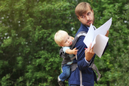 businessman with his son in a sling on back, show him contract documents, baby wants to take red pen, copy spaceの写真素材