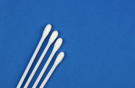four white cotton swabs or buds for personal hygiene or for treatment of wounds, on blue background, close-upの写真素材
