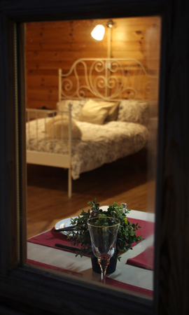 spy view through window of wooden country house, made bed, set table for a romantic dinner, a glass of wine, plates and nightlight, secret rendezvousの写真素材