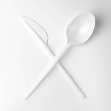 clean white plastic crossed kitchen spoon and knife on white background, ecological problem, closeup, square photoの写真素材