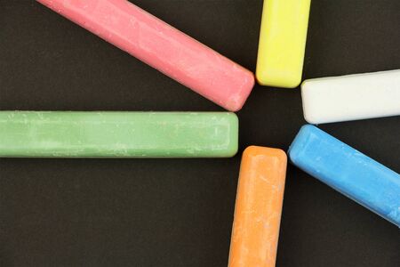six colored children crayons on black background, different colors chalks for school or preschool activities, blue red green yellow orange white, in shape of sun, top viewの写真素材