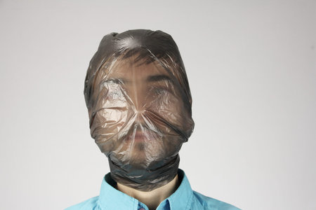 black plastic bag wraps around a human head, gray background, concept of suffocating person, big...