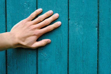 human hand palm on vertical green wooden planks with peeling paint, texture and background close-up