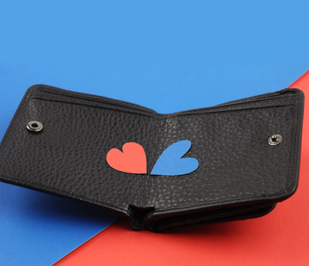 black leather wallet with two craft paper hearts red and blue on color papers background, side view,...