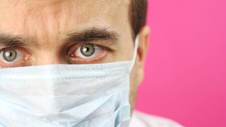 close-up face with medical mask on pink background, serious research scientist doctor looks intently and carefully, search or development vaccine against virus or coronavirusの写真素材