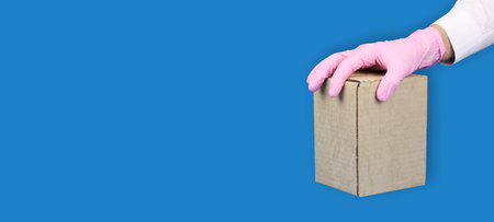 hand in pink medical glove holds cardboard box on top, concept of safety mail goods courier delivery...