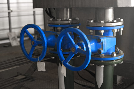 two big blue tap or valve or faucet on water pipe on gray industrial background, inside wastewater...