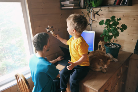 father freelancer try work from home office in quarantine, child with cat sits near and plays,...