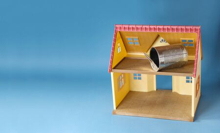 empty used tin can inside toy house on blue background, garbage concept zero waste, trash accumulation from food packages, environment pollution or home contamination problem, copy spaceの写真素材