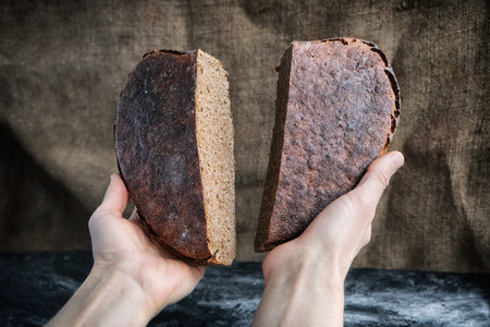 baker hold in hands two parts of loaf rye whole grain yeast-free sourdough bread in shape of heart...