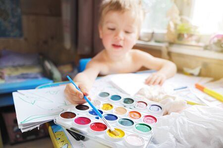 Small child sit at desk and draw with watercolors and paint brush in quarantine isolationの写真素材