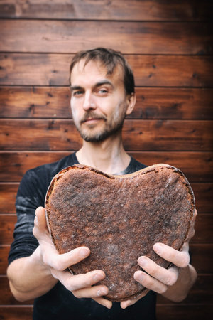 Baker holding in hands vegan rye whole grain yeast-free sourdough bread in shape of heart