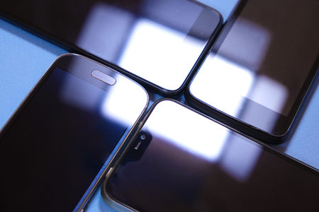 set of four black different smartphones on blue background with square light flare, concept of...
