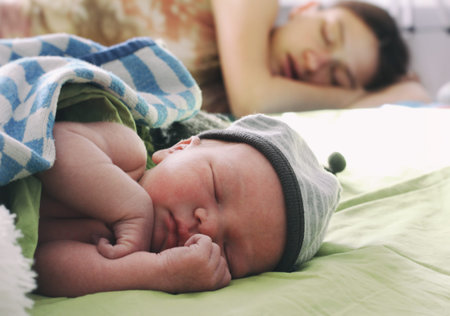 newborn baby and his tired exhausted mother sweetly sleep and relax together in bed, concept of silence and dreams, difficulties of motherhood  の写真素材