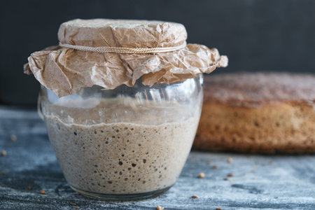 Fresh sourdough on whole grain flour in glass jar and rye bread on blackの写真素材