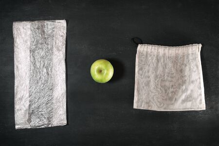 fresh green apple between plastic package and eco grocery mesh, comparison of disposable and reusable packages, concept of conscious consumerism, mindful sustainable living and environment pollution の写真素材