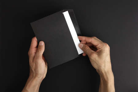 male hands holding blank black envelope with white letter on black background, receive good message and read, open mail, mockup with copy spaceの写真素材