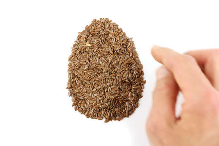 human hand arranged flax seeds in egg shape, replacing eggs in vegan or vegetarian recipe, close up view on white background, top view, veganism cookingの写真素材
