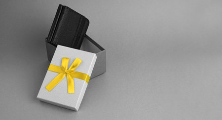 open gray gift box with yellow ribbon bow with new leather wallet on gray paper background, business present or surprise in trendy coolors for birthday or greeting holidays, banner with copy spaceの写真素材